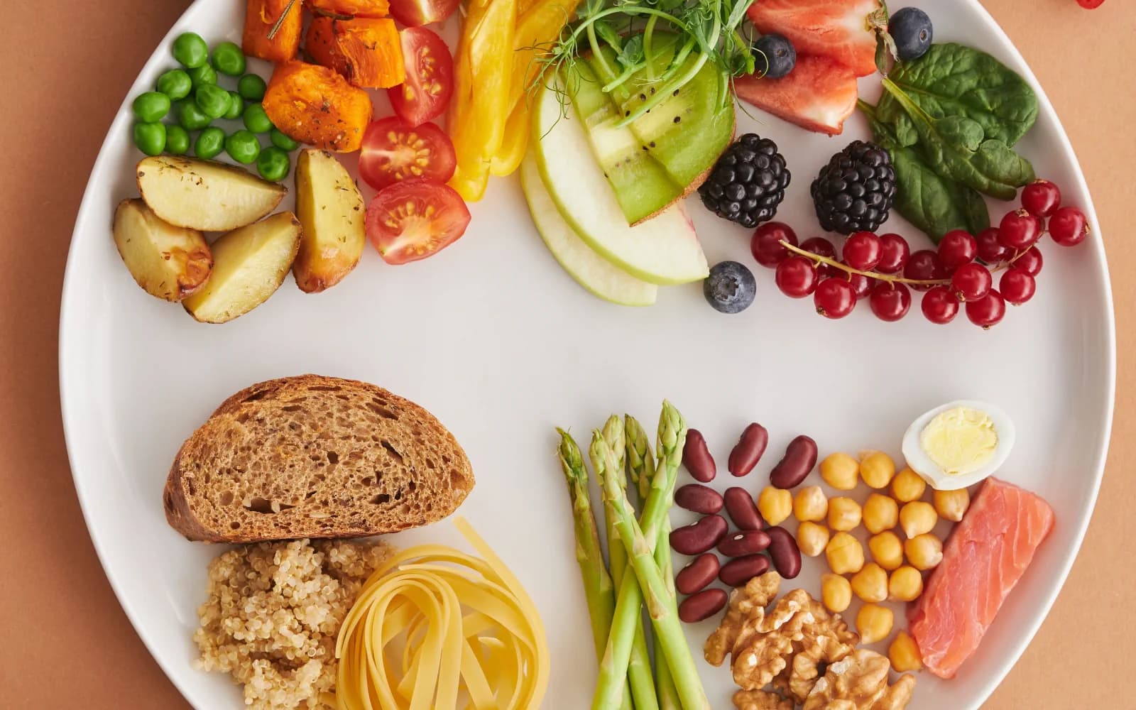 Seleção de frutas, legumes, grãos e nozes disposta sobre uma mesa clara.