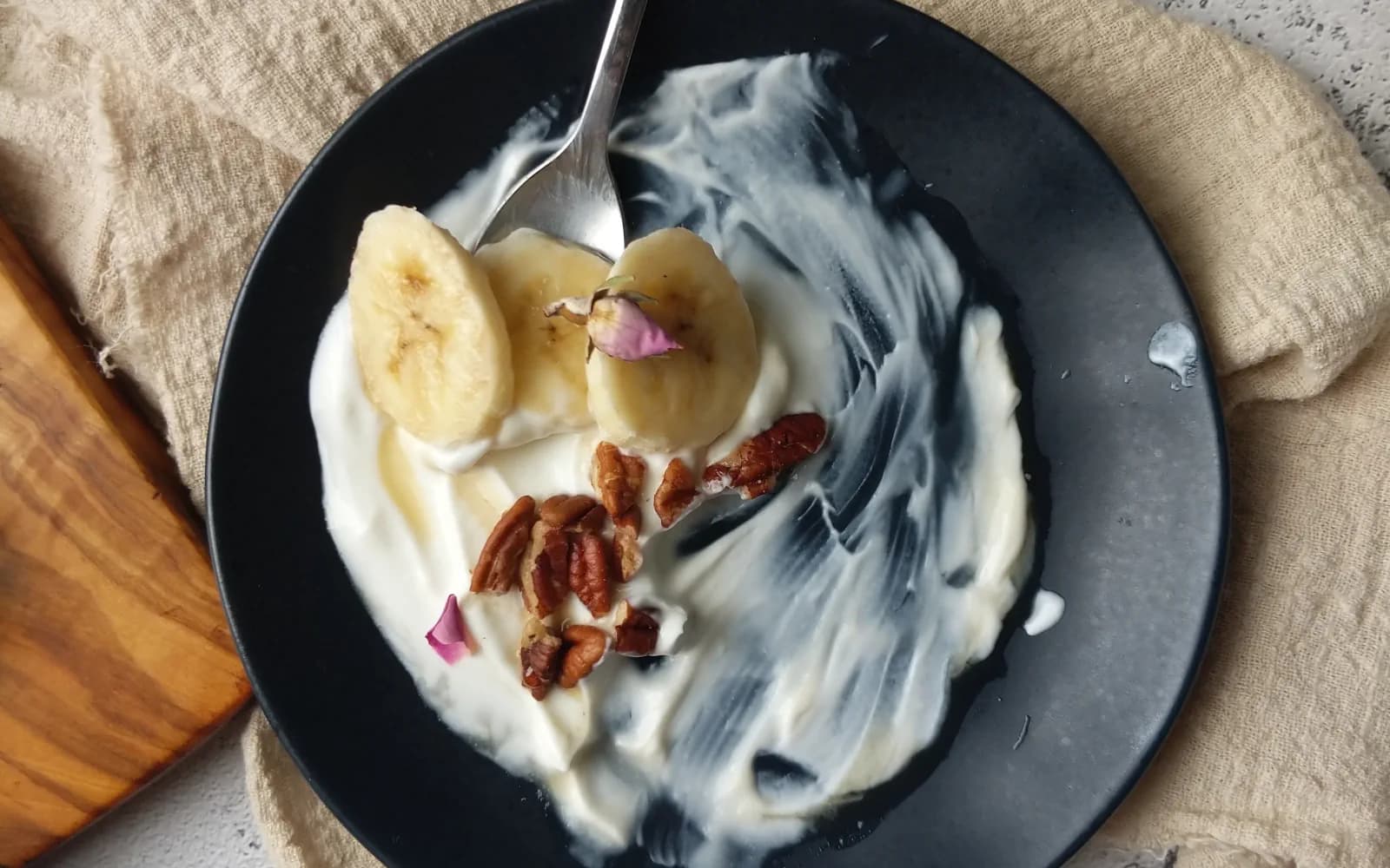 Iogurte com rodelas de banana e nozes servido em um prato de cerâmica.